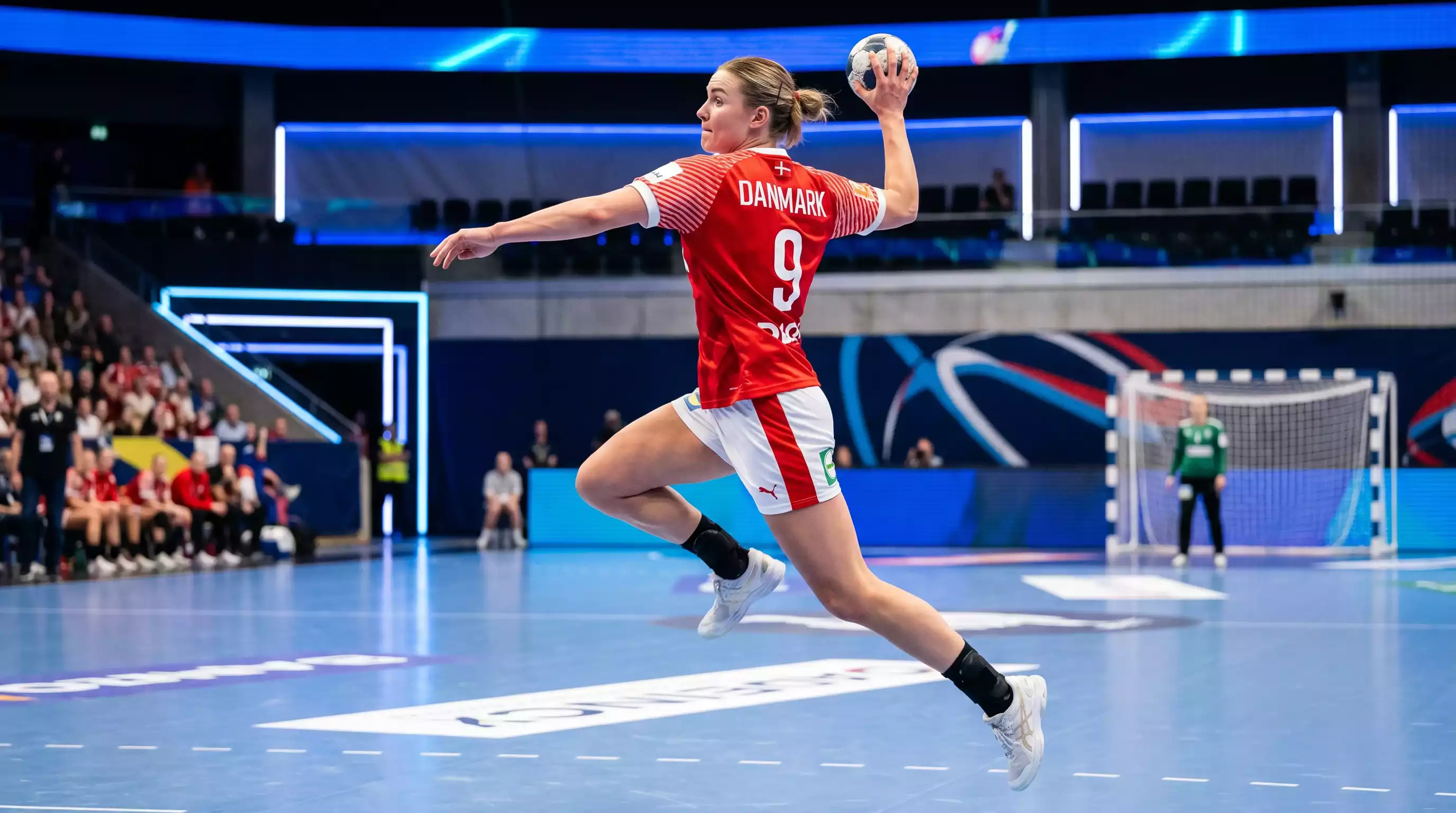 Moderne håndboldspiller i dansk landsholdstrøje kaster mod mål i oplyst arena